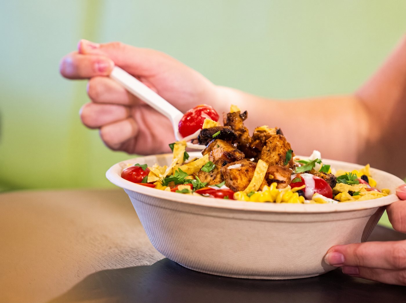 A guest lifting a forkful from a CoreLife Eatery bowl of grilled chicken, corn, tomatoes and tortilla strips