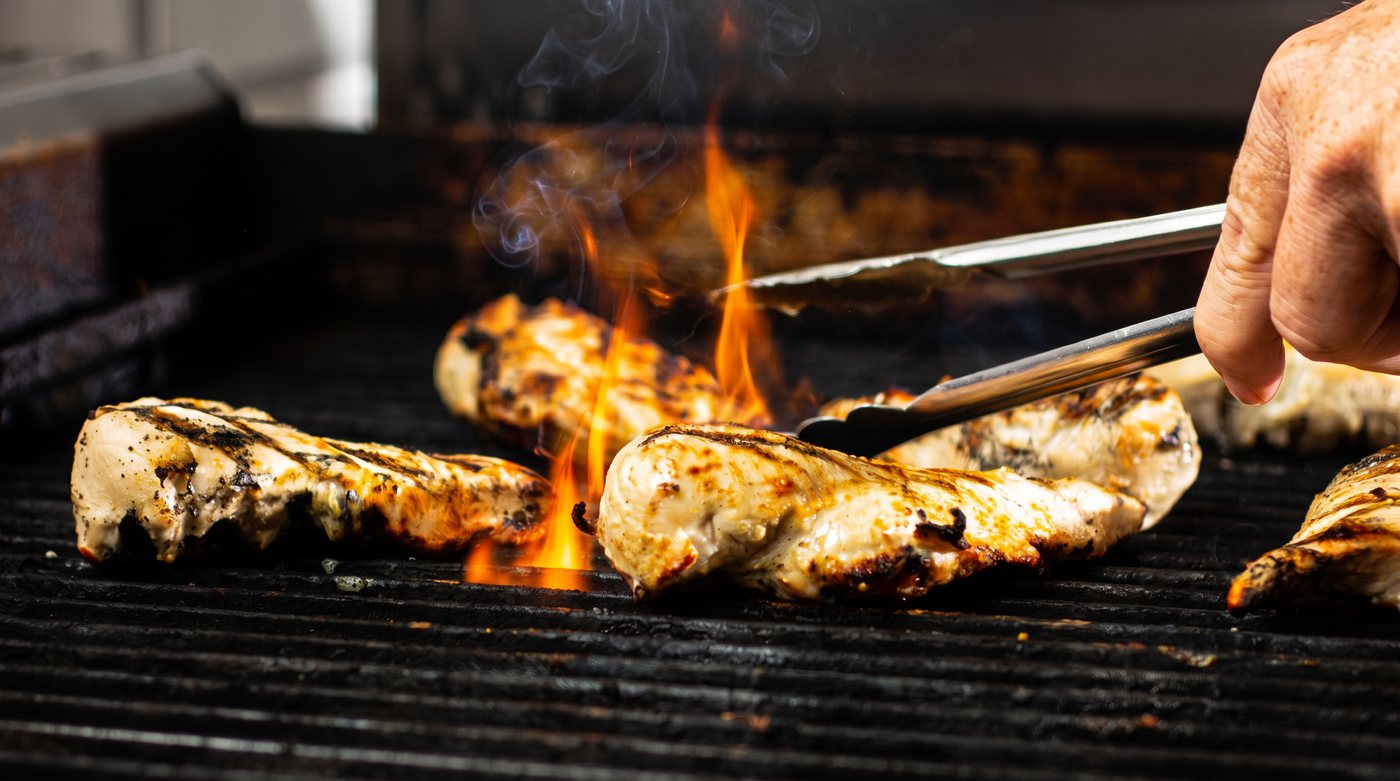 Chicken breasts being turned with tongs on the open grill in a CoreLife Eatery kitchen